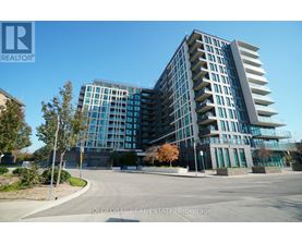 A modern multi-story building with a glass facade and a parking lot in front.