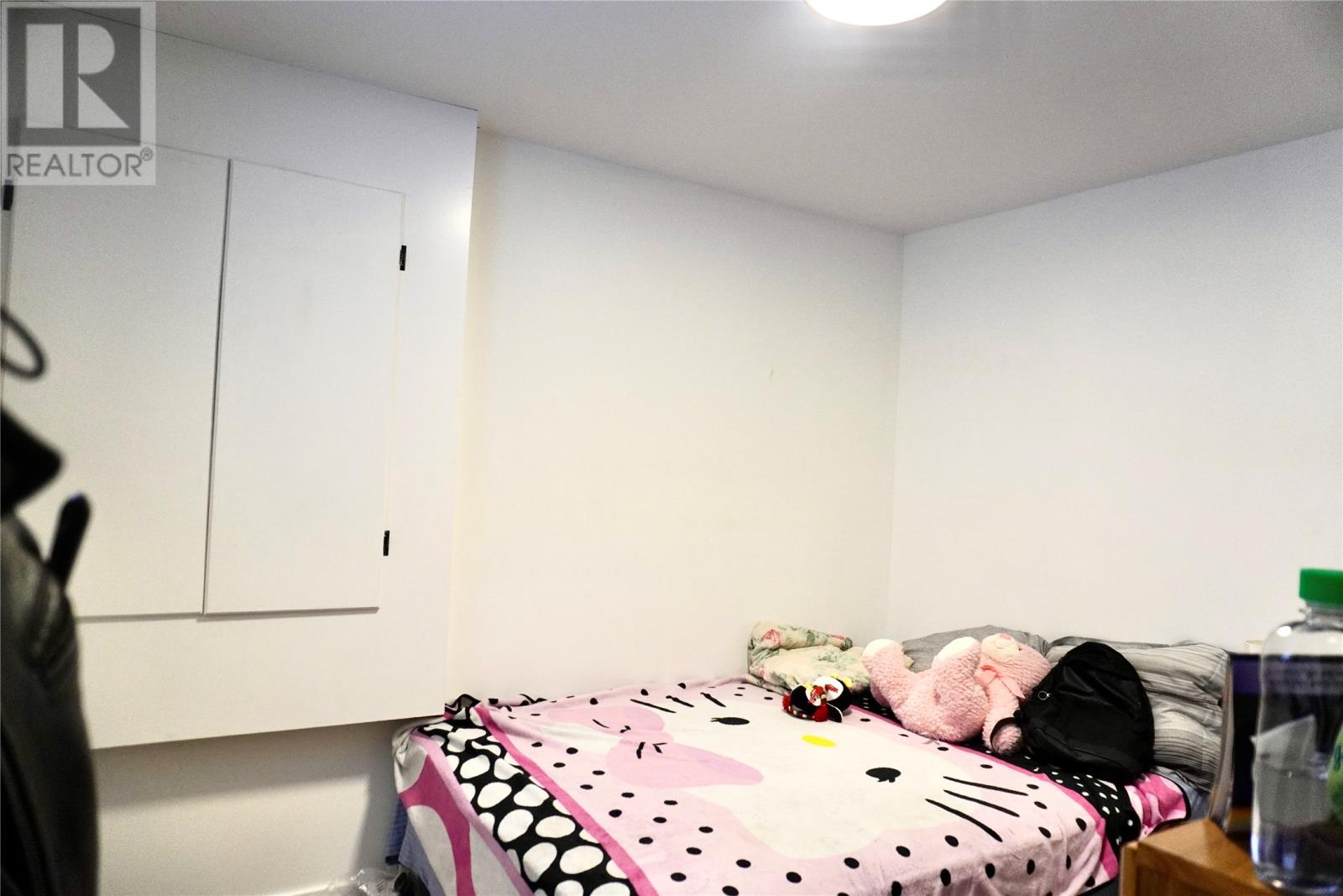 A bedroom with a bed covered in a Hello Kitty print blanket and a white wall.