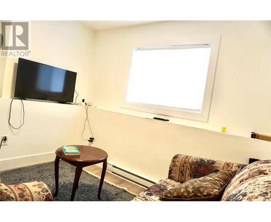 A living room with a couch, a table, and a flat screen TV mounted on the wall.