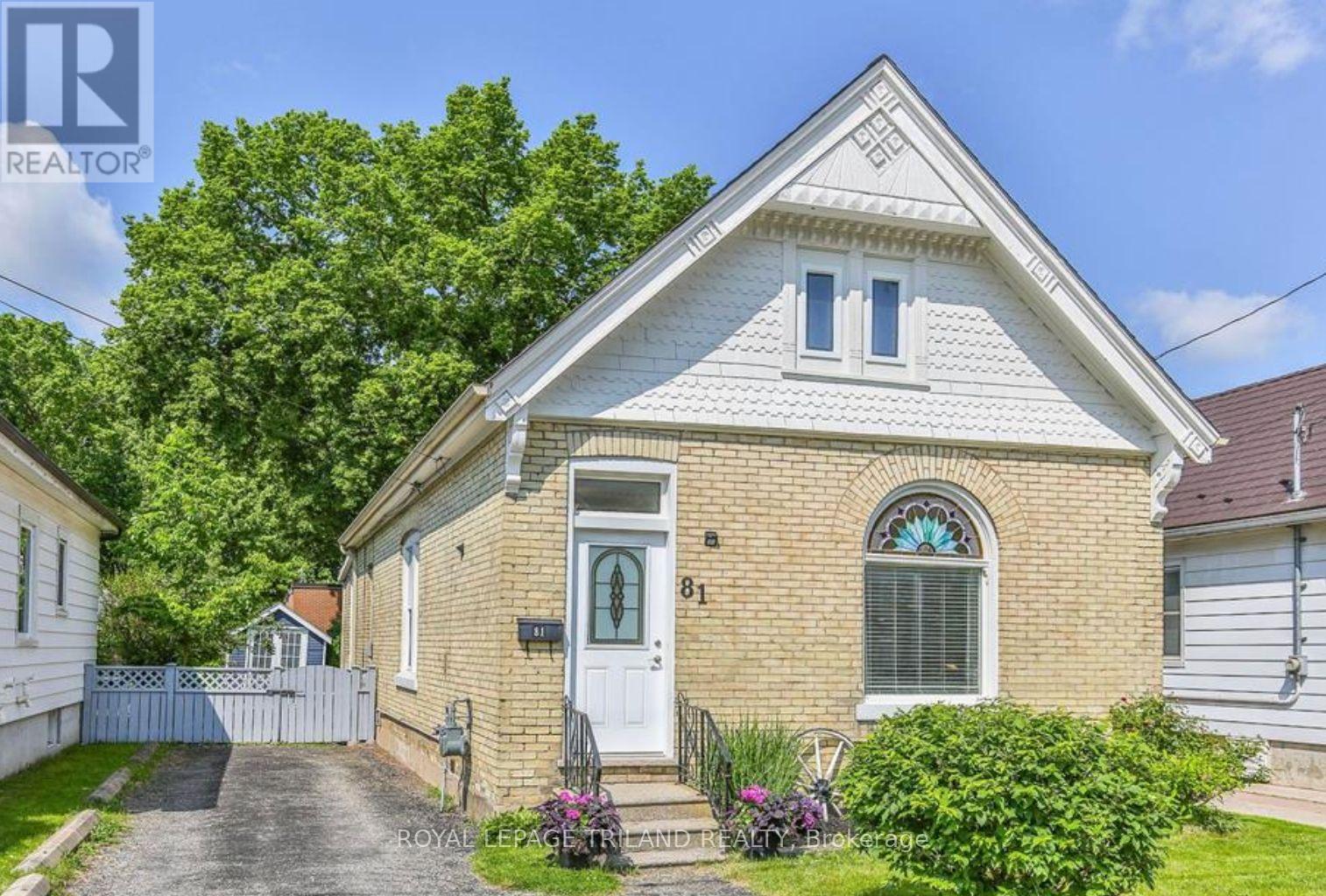 A house with a white door and a brick facade is surrounded by greenery.