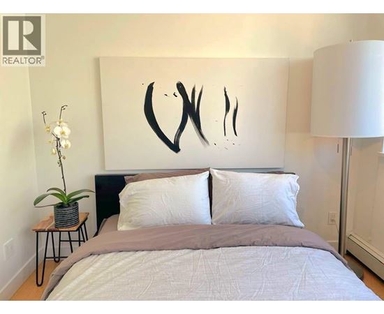 A bedroom with a large bed and a large abstract painting on the wall.