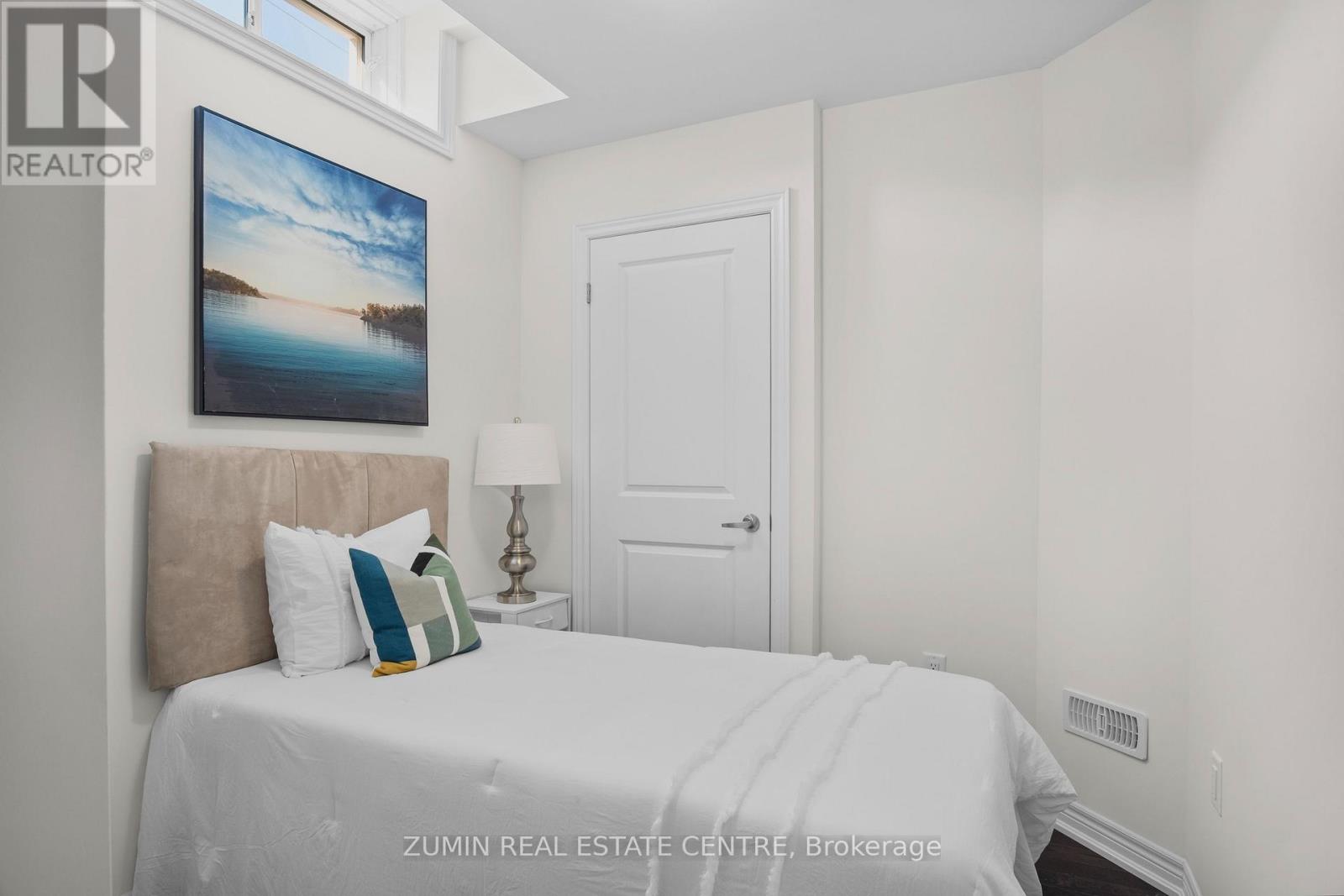 A bedroom with a bed, pillows, a lamp, and a painting on the wall.