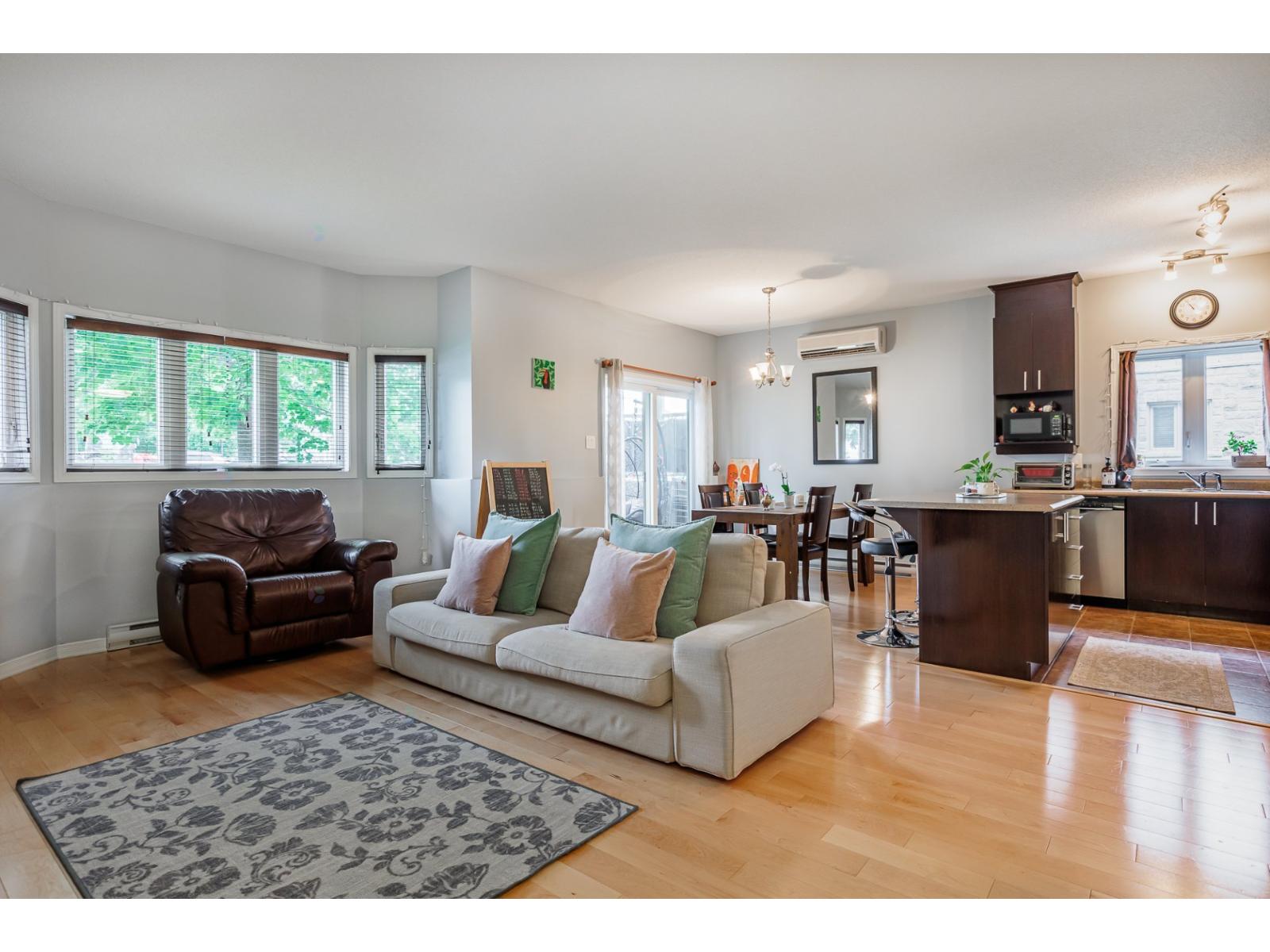 A living room with a brown leather chair, a white couch with green pillows, and a grey rug.