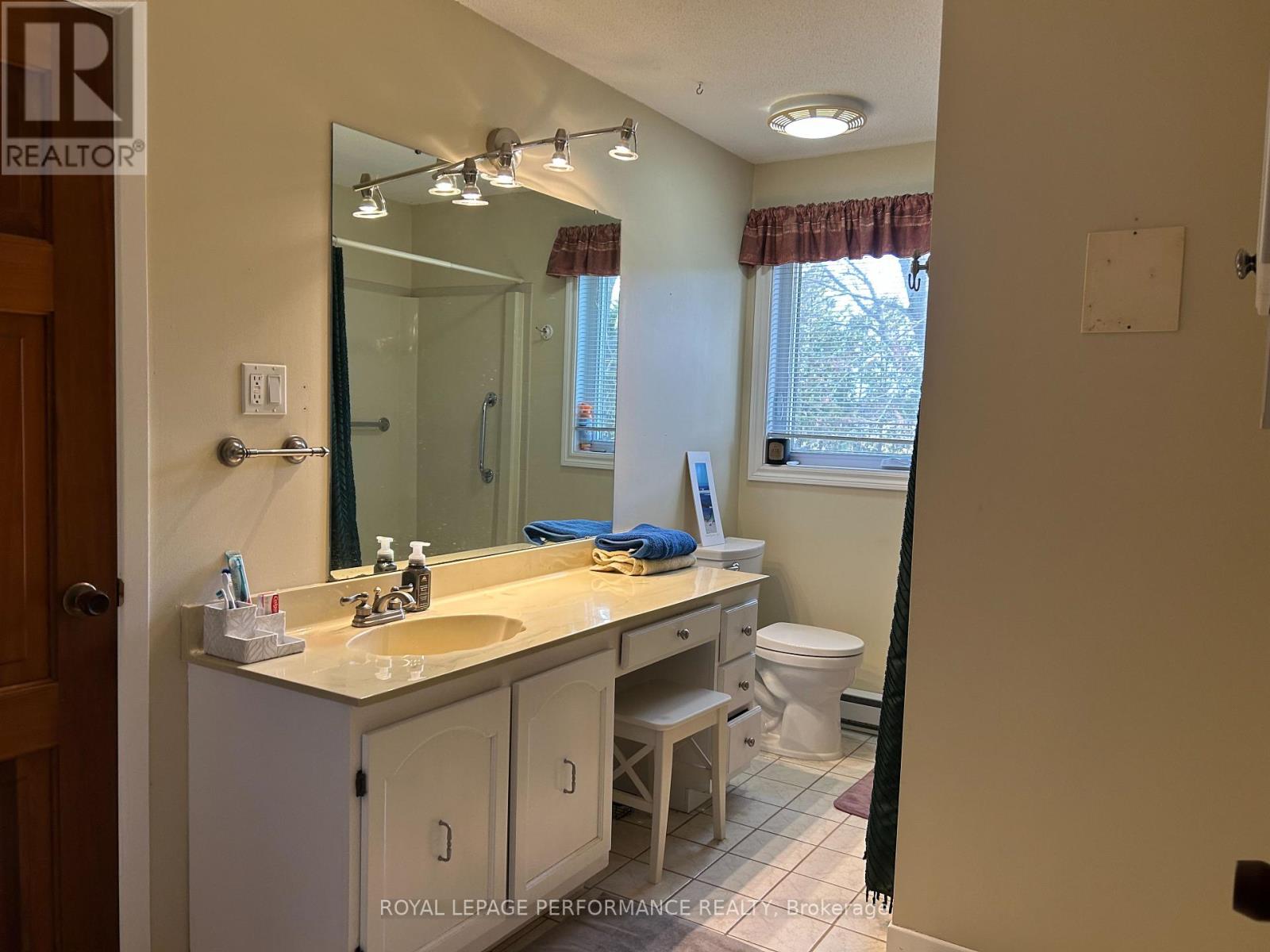A bathroom with a sink, mirror, toilet, and a window.
