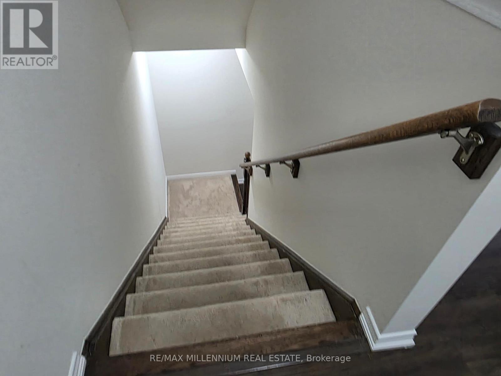 A staircase with a wooden handrail and beige carpeted steps.