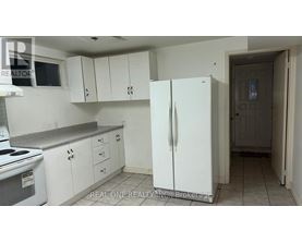 A white refrigerator stands in a kitchen with white cabinets and a white stove.