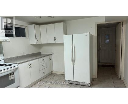 A white refrigerator stands in a kitchen with white cabinets and a white stove.