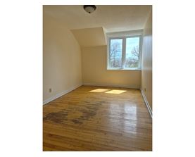 A room with wooden floors and a window showing trees outside.