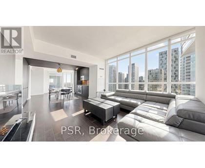 A modern living room with a large grey sofa and a view of the city.