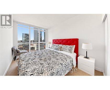 A bedroom with a large bed and a city view through the window.