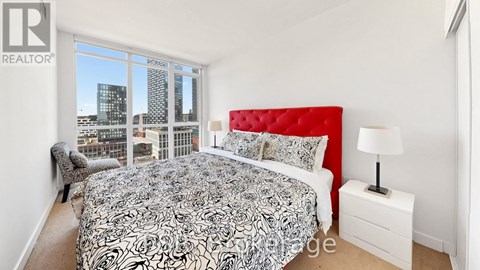 A bedroom with a large bed and a city view through the window.