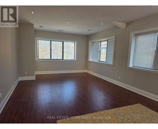A room with wood flooring and two windows.