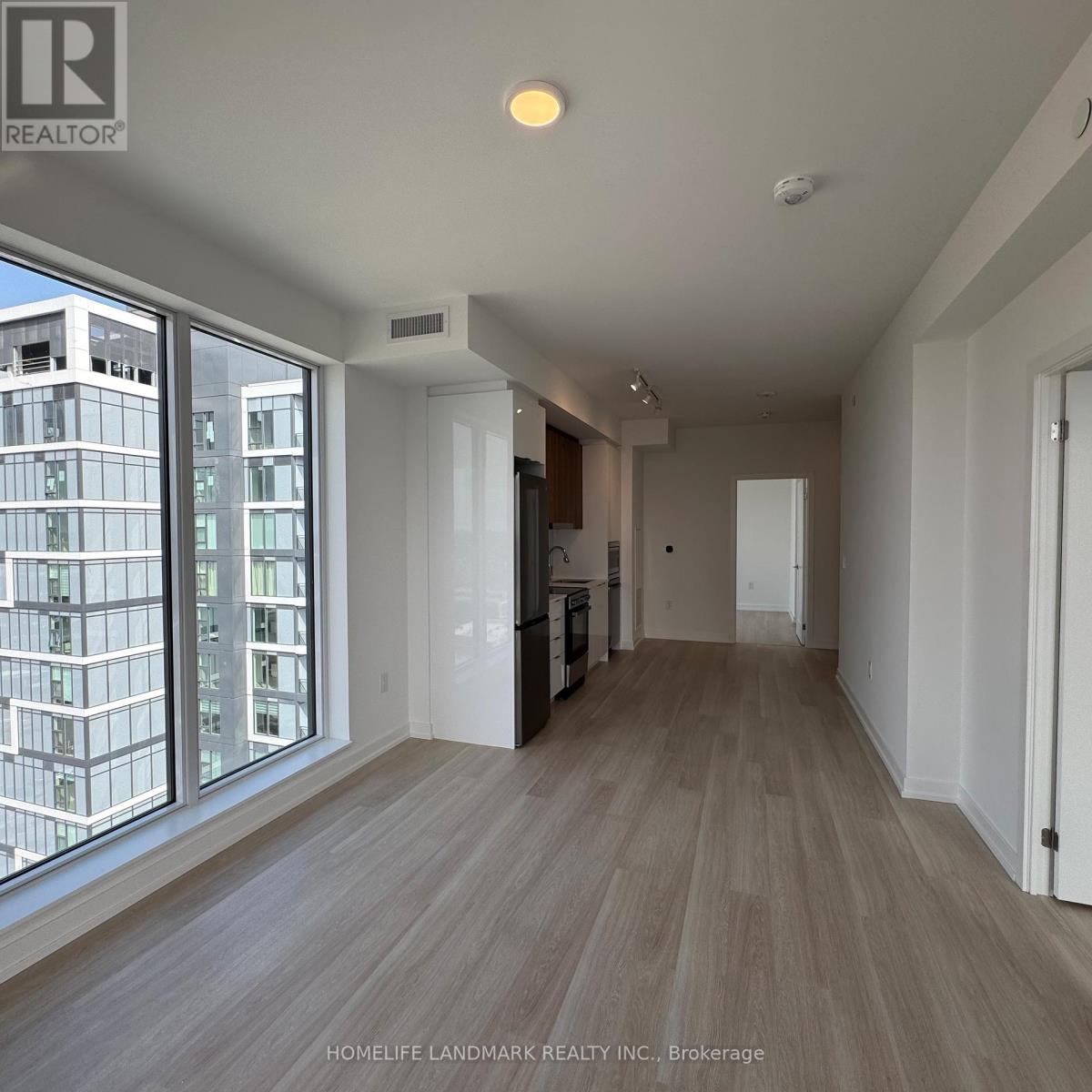 A spacious room with wooden flooring and large windows overlooking a cityscape.