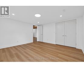 A room with white walls and wooden flooring, with a logo in the top left corner that reads "REALTOR".