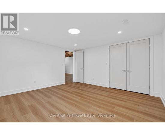 A room with white walls and wooden flooring, with a logo in the top left corner that reads "REALTOR".