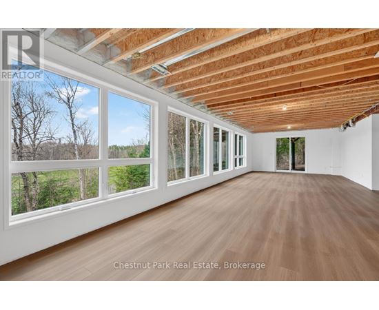A room with wooden floors and a large window overlooking a wooded area.