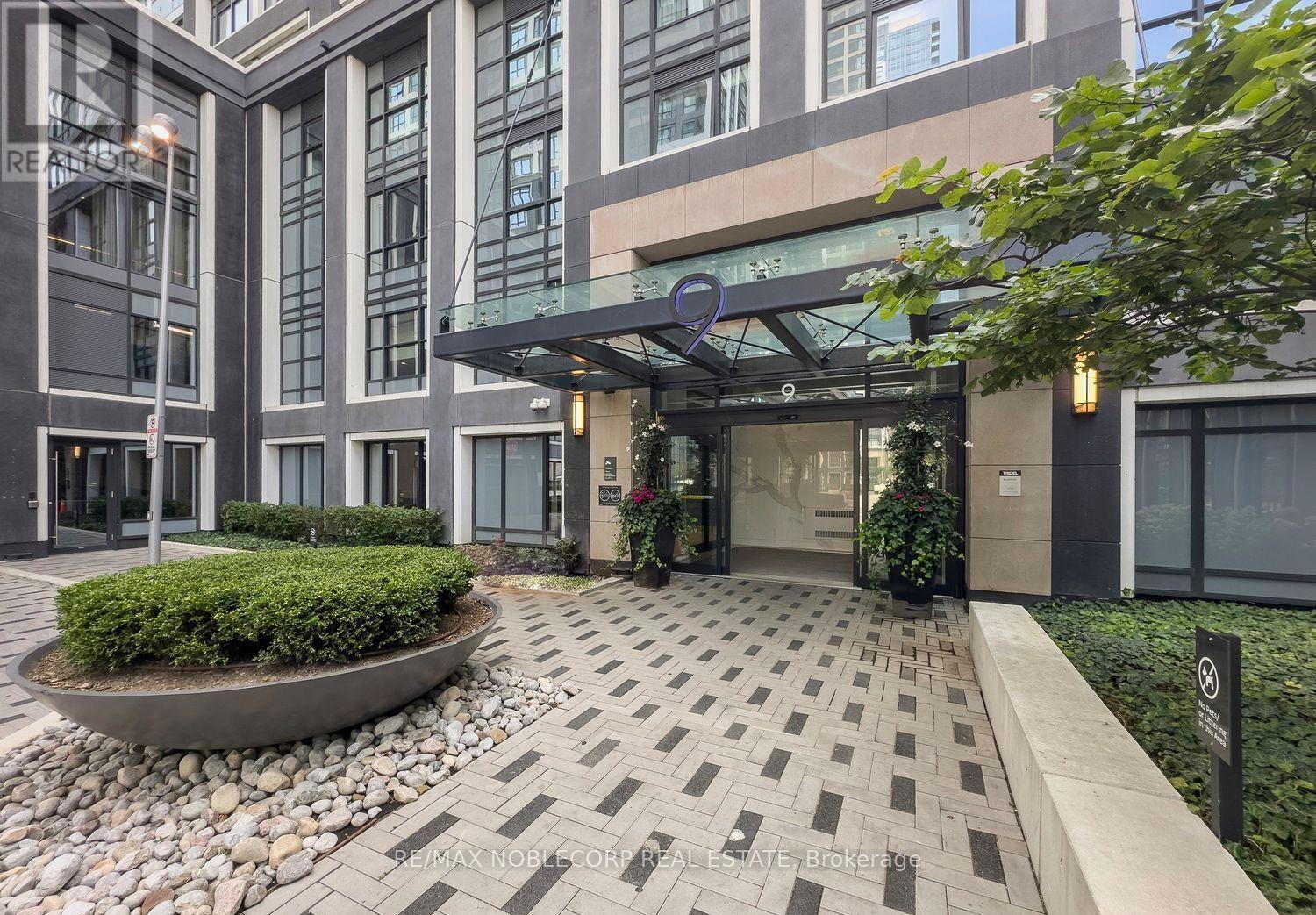 The entrance to a building with a glass door and a small garden in front.