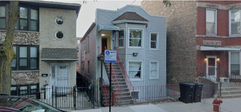 A grey house with a black fence and a red fire hydrant in front.
