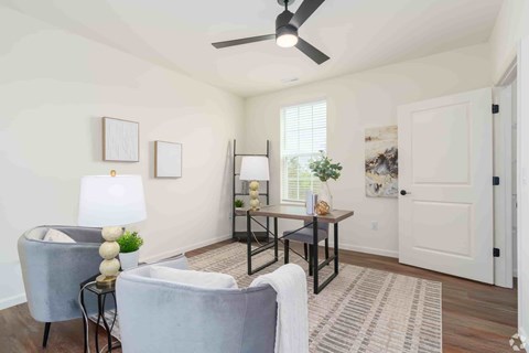 A living room with a grey couch, a table with a vase and a plant, and a ceiling fan.