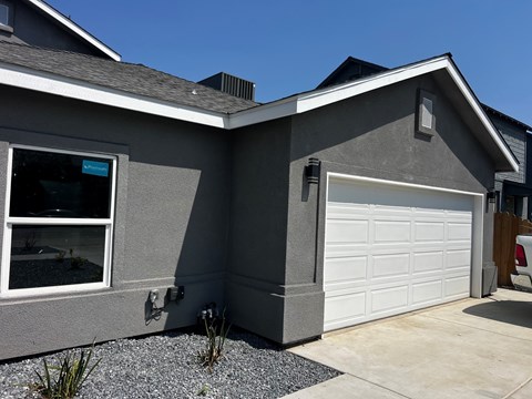 A grey house with a white garage door and a window showing a view of a backyard.