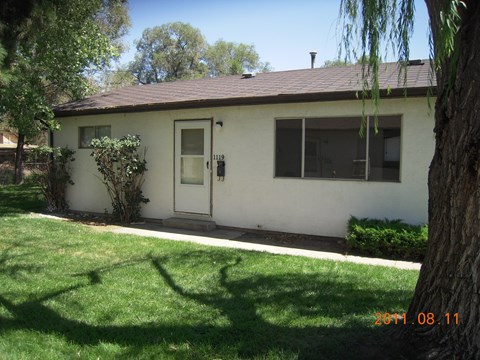 A white house with a brown roof and a tree in front of it.
