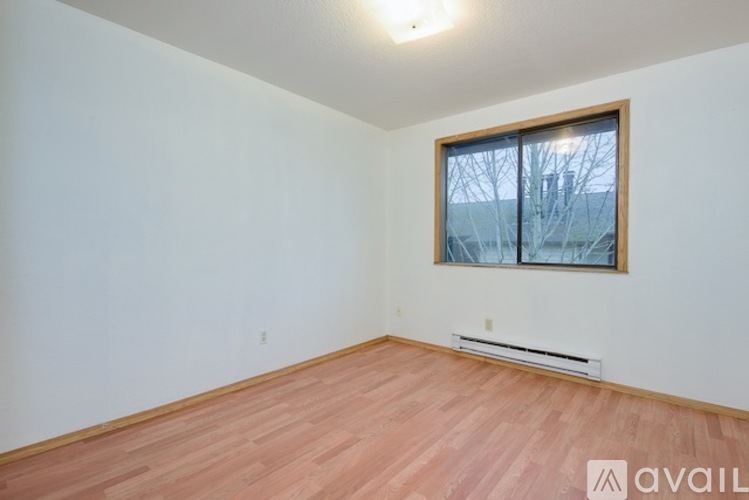 A room with wooden flooring and a window with a view of a building outside.