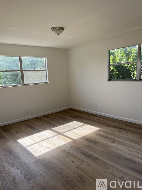 A room with wooden flooring and a window letting in sunlight.