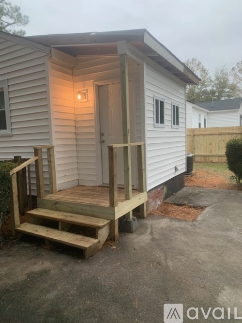A small white house with a wooden deck and steps leading to the door.