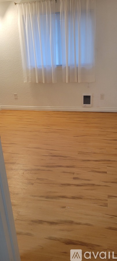 A room with wooden flooring and a window with curtains.