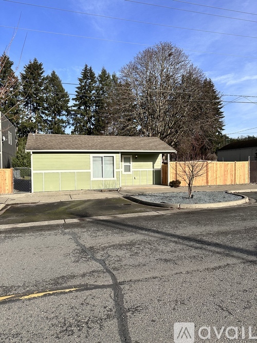 A house with a green front and a brown roof is surrounded by a fence.