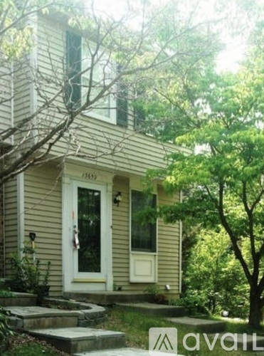 A house with a white door and a window is surrounded by trees.