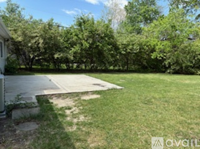 A backyard with a concrete patio and a white house.