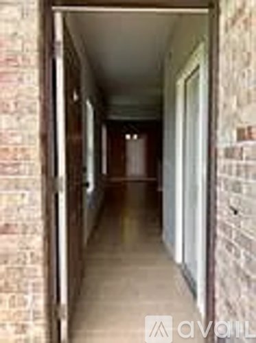 A long hallway with a brick wall on the left and a white door on the right.