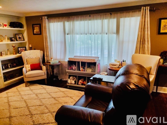 A living room with a brown leather chair and a white chair with a red pillow.