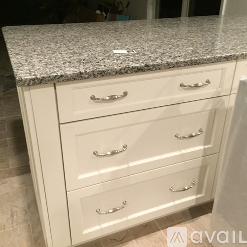 A kitchen counter with a granite top and white drawers.