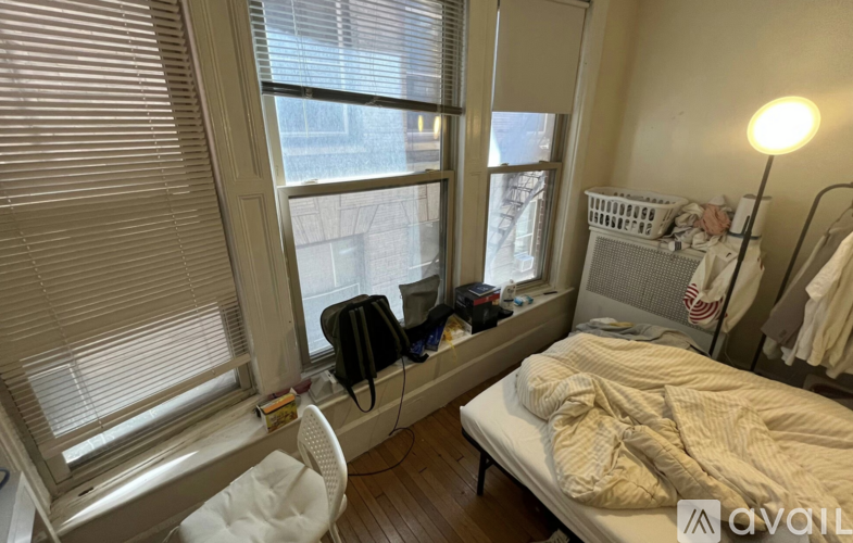 A bedroom with a bed, chair, and window with blinds.