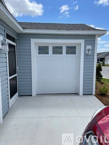 A white garage door is closed and there is a red car parked in front of it.