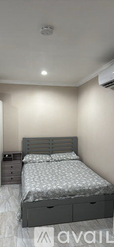 A bedroom with a bed, nightstand, and a smoke detector on the ceiling.