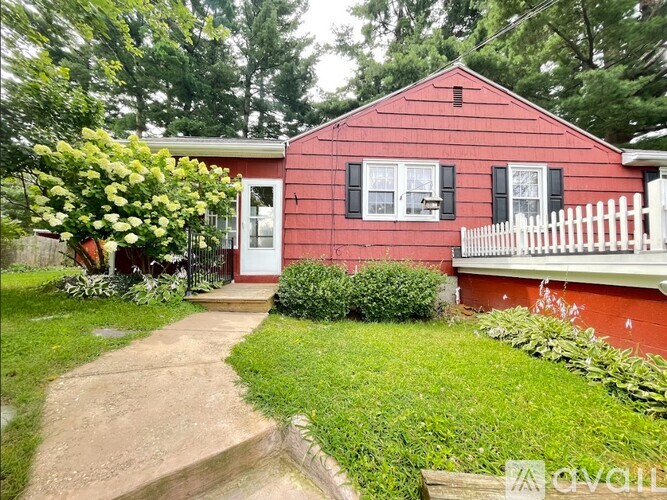 A red house with a white picket fence and green bushes in front.