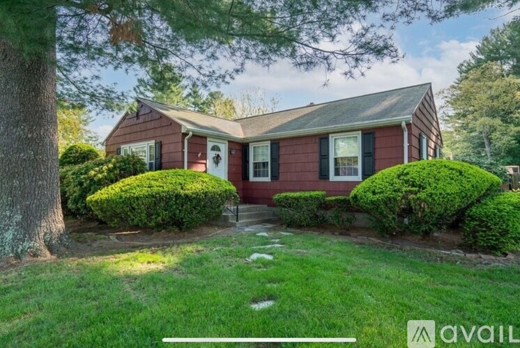 A house with a red exterior is surrounded by greenery and has a white door and windows.