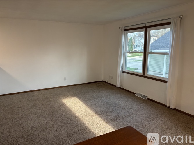 A room with a carpeted floor and a window overlooking a residential area.