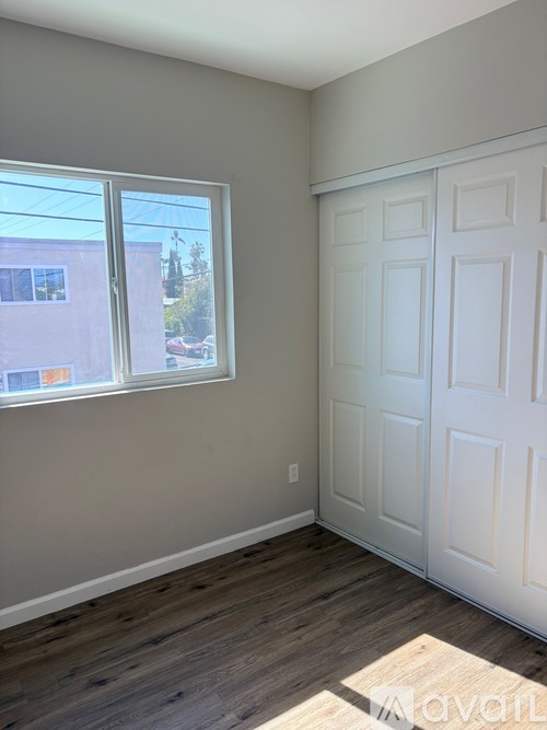 A room with a white door and a window with a view of a building and trees outside.