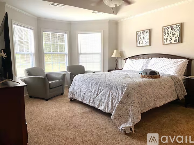 A bedroom with a large bed, two chairs, and a ceiling fan.