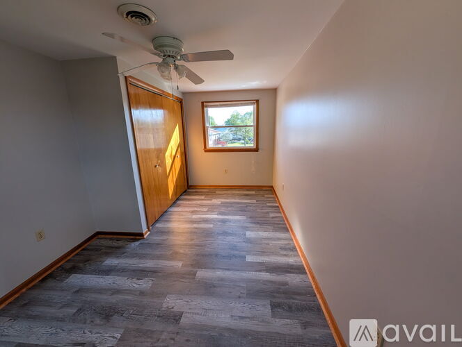 A room with a ceiling fan and a window with a view of trees.