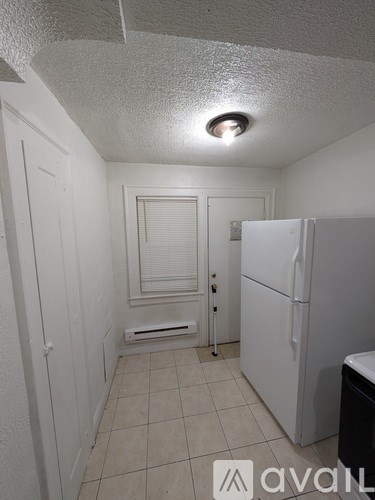A small, white refrigerator sits in a narrow kitchen.