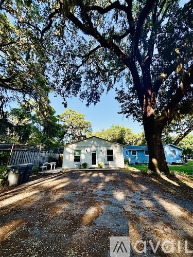 A house is surrounded by trees and has a dirt driveway.