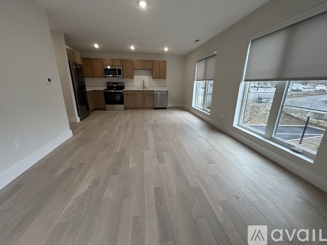 A spacious living room with wooden flooring and a kitchen area in the background.