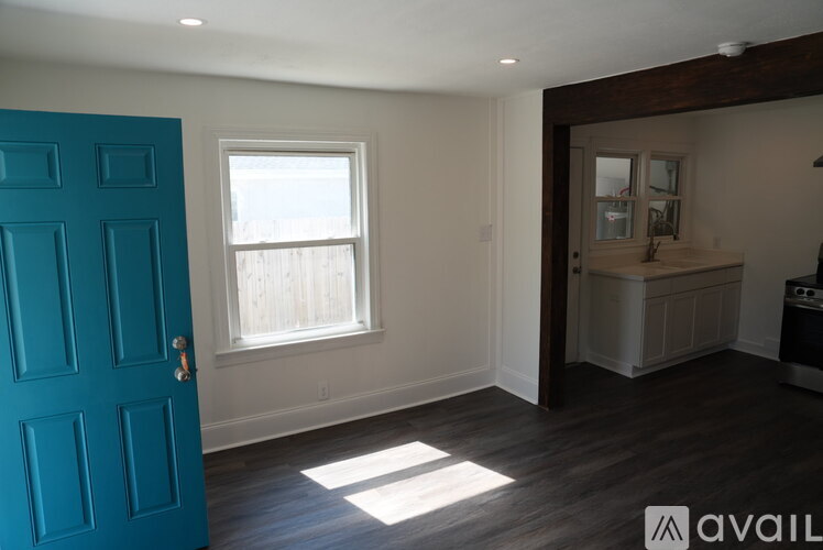 A room with a blue door, a window, and a wooden floor.