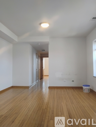 A room with wooden floors and white walls, with a door at the end of the hallway.