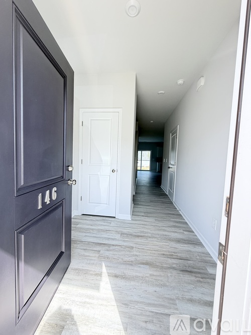 A hallway with a dark door on the left and a white door in the distance.